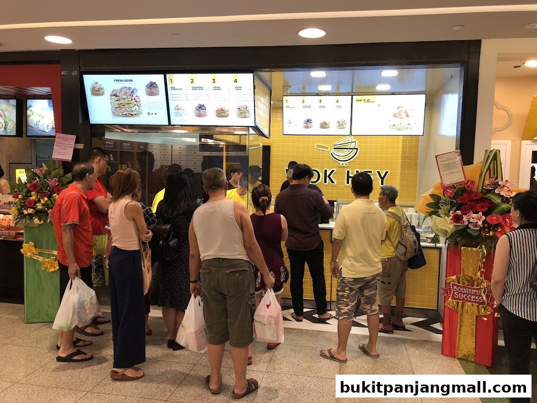 Customers queue at WOK HEY Bukit Panjang Plaza, with digital menus displaying food options.