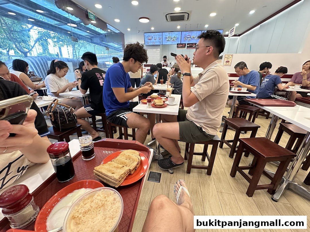 People enjoying traditional breakfast at Ya Kun Kaya Toast, with kaya toast and coffee visible.