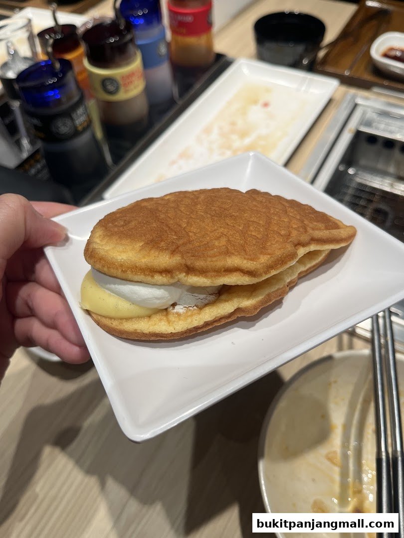 A hand holds a dessert pancake with cream and custard filling on a white plate.