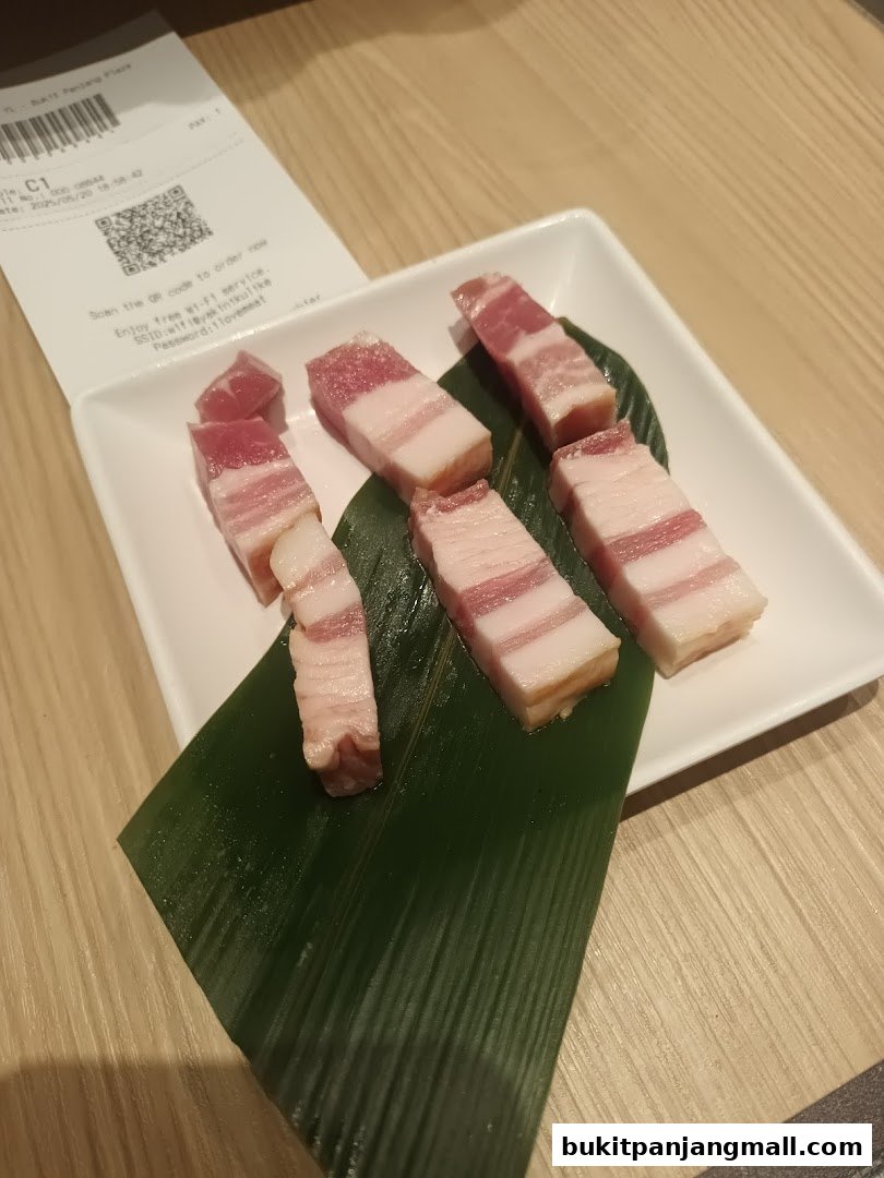 Slices of raw pork belly are arranged on a white plate with a green leaf.