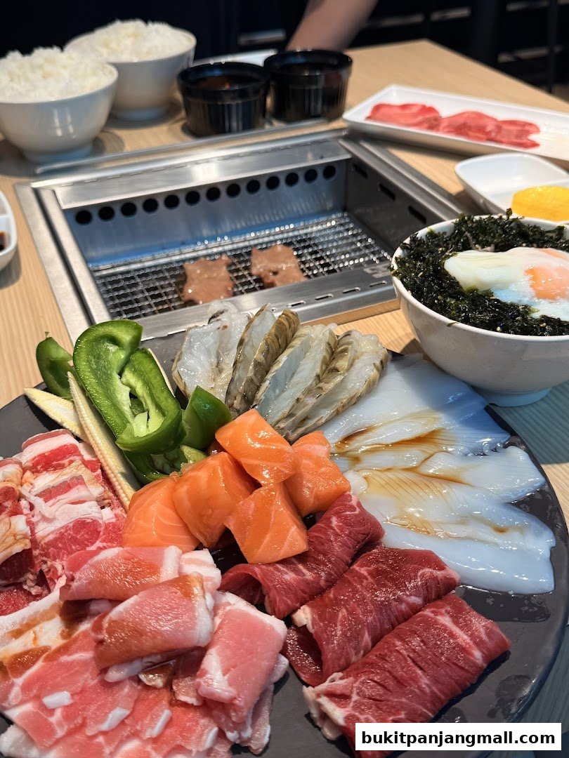A platter of assorted raw meats, seafood, and vegetables for grilling, with rice and dipping sauces.