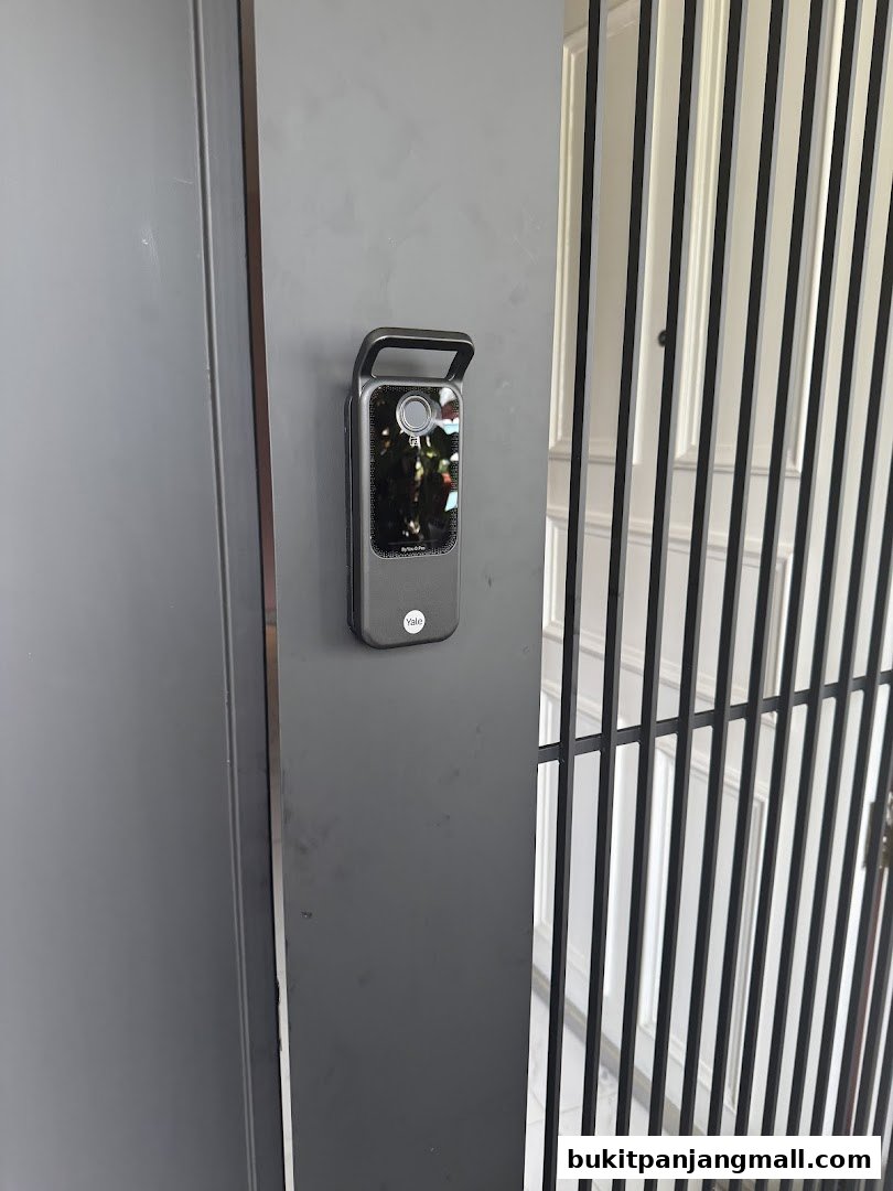 A close-up of a Yale smart lock on a grey door next to a metal gate.