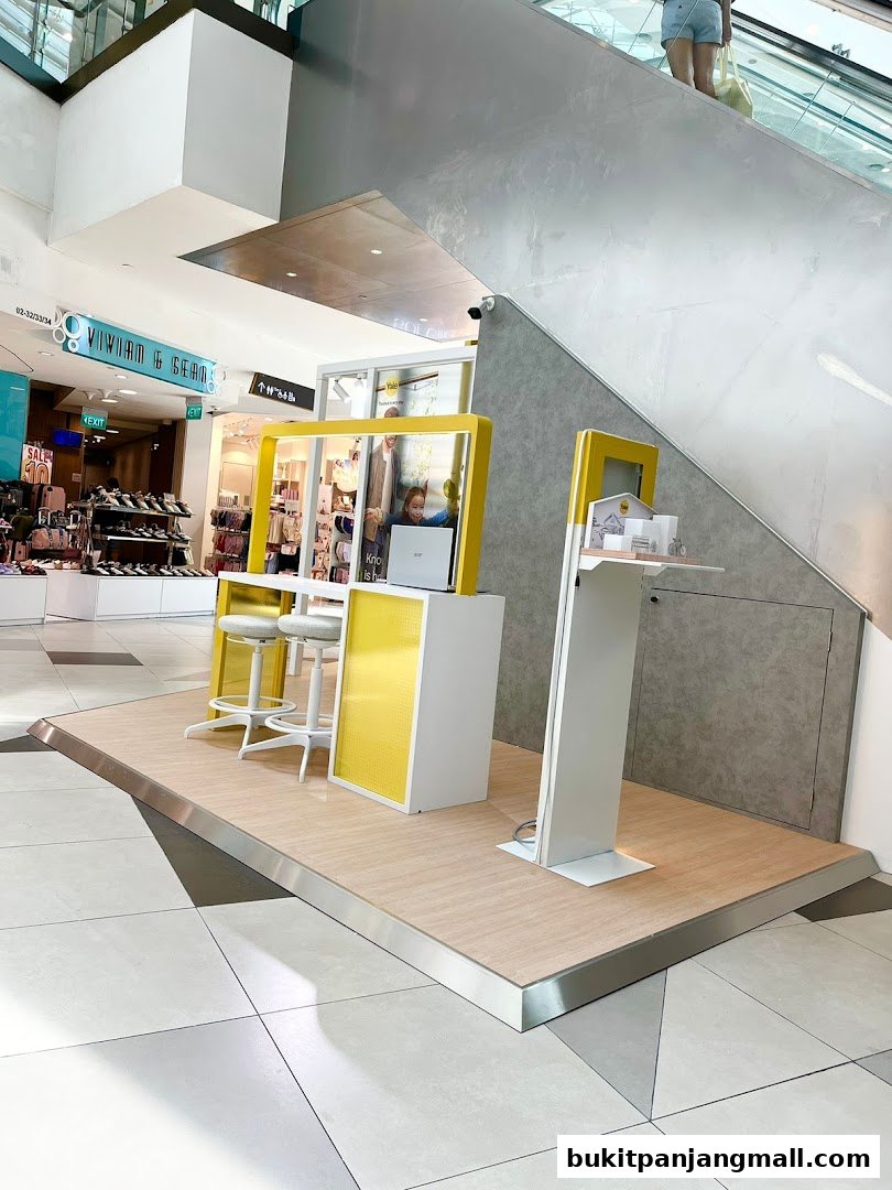 A modern retail display with yellow accents and seating, featuring a laptop and products.