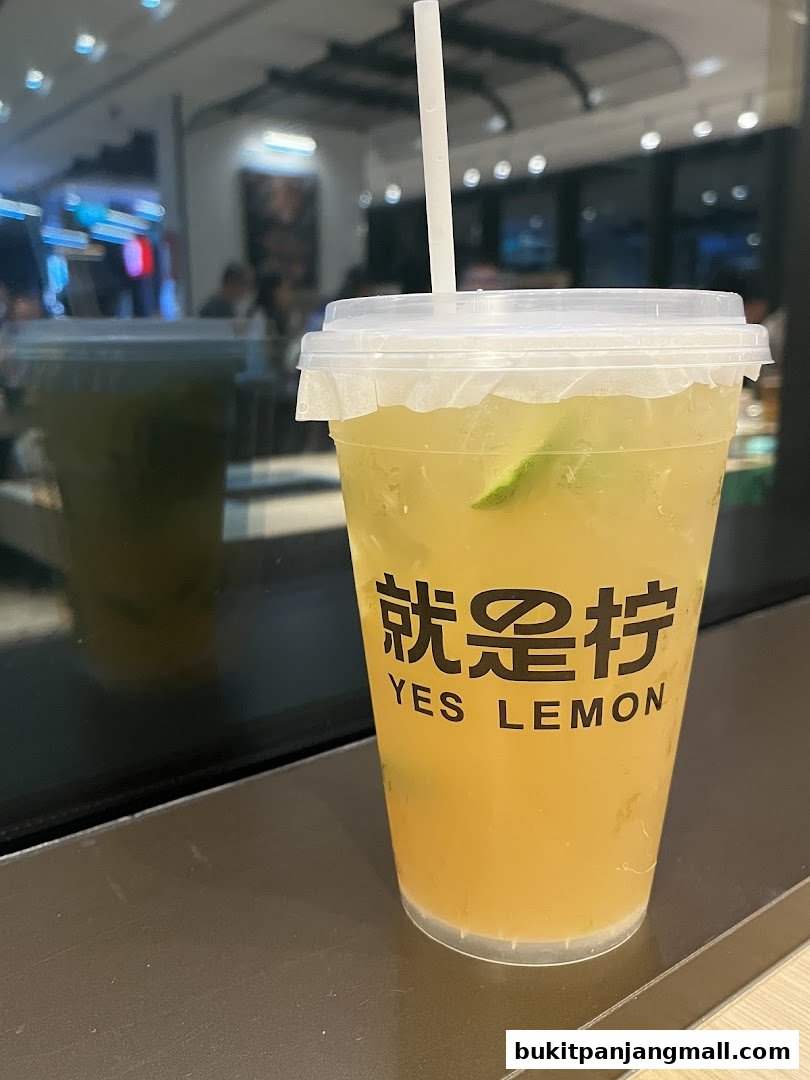 A refreshing lemon drink with lime slices in a clear plastic cup with the shop's logo.