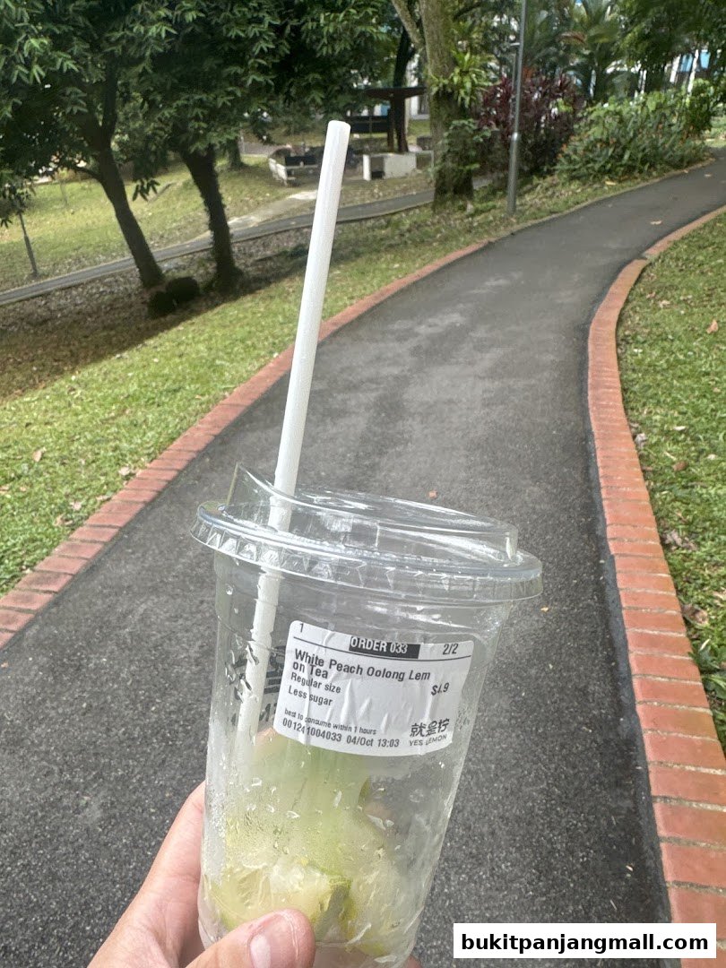 A hand holds a nearly empty plastic cup with a straw, showing a drink label.