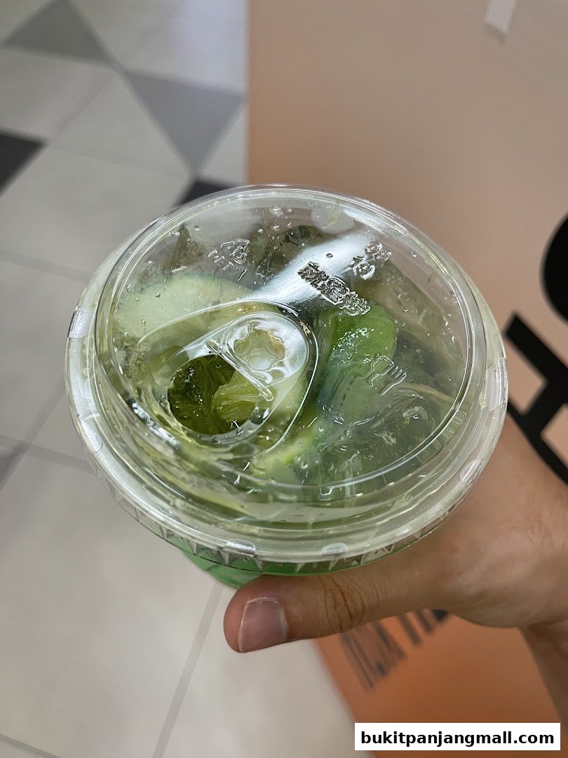 A hand holds a clear plastic cup filled with a green beverage and ice.