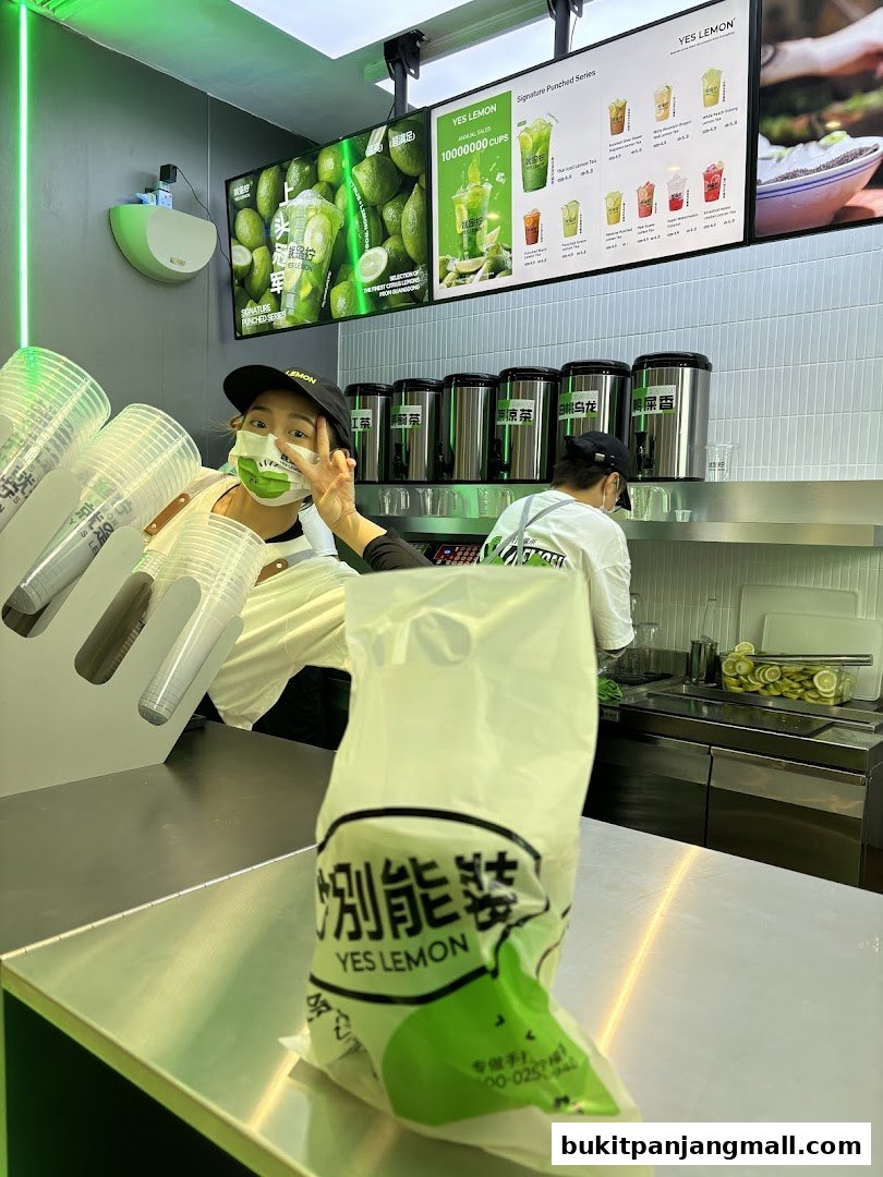A smiling staff member at a Yes Lemon beverage shop, with drinks and menu displayed.