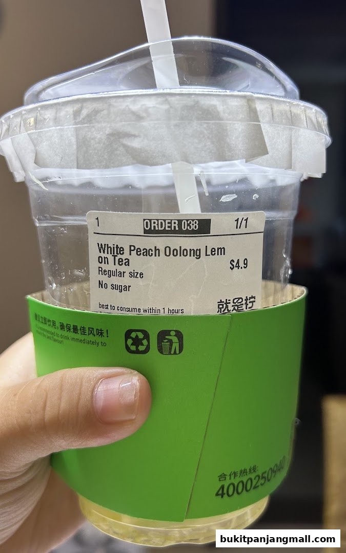 A hand holds a cup of White Peach Oolong Lemon Tea with a green sleeve.